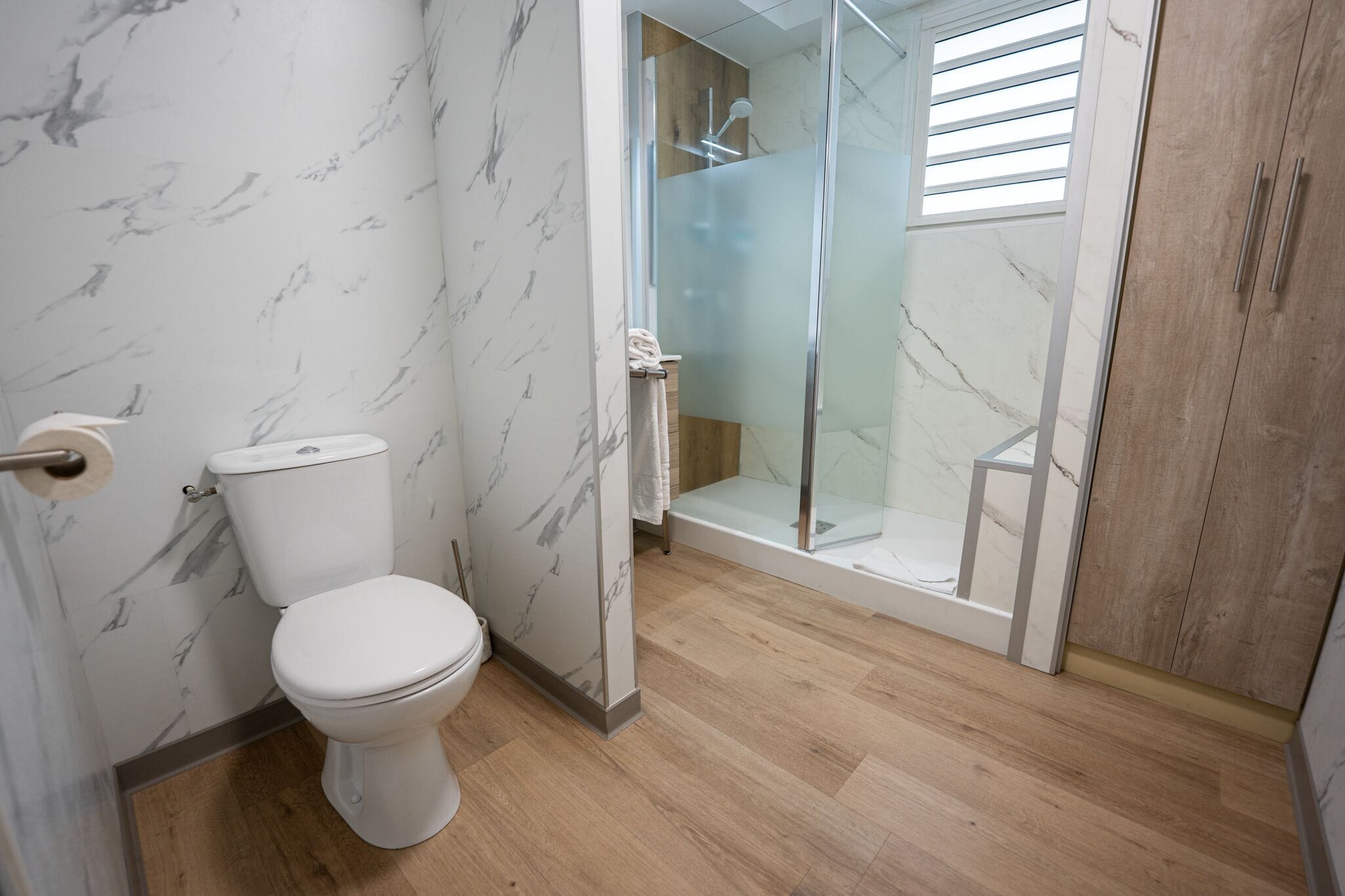 Un baño con inodoro, cabina de ducha de cristal y suelo de madera.