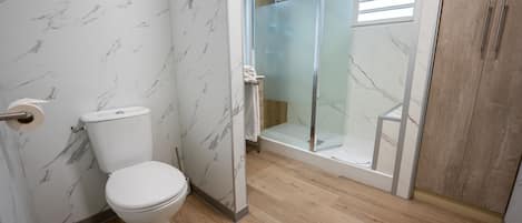 Un baño con inodoro, cabina de ducha de cristal y suelo de madera.