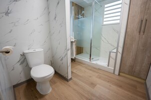 Un baño con inodoro, cabina de ducha de cristal y suelo de madera.