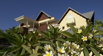 Una casa moderna de dos pisos con un balcón y un pequeño jardín con plantas florecientes.