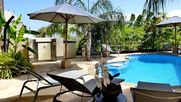 Zona de piscina con sillones de descanso, sombrillas y una orquídea en maceta.