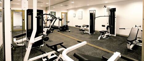 Un gimnasio con diverso equipamiento de ejercicio, que incluye cintas de correr, máquinas de pesas y pesas libres.