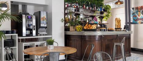 A modern kitchen with a bar area, equipped with a coffee machine, wine bottles, and a variety of kitchen utensils.