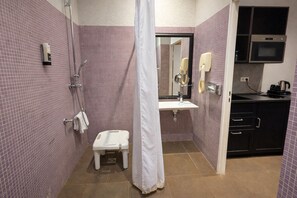 Een badkamer met douche, toilet, wastafel en een klein keukentje met oven.