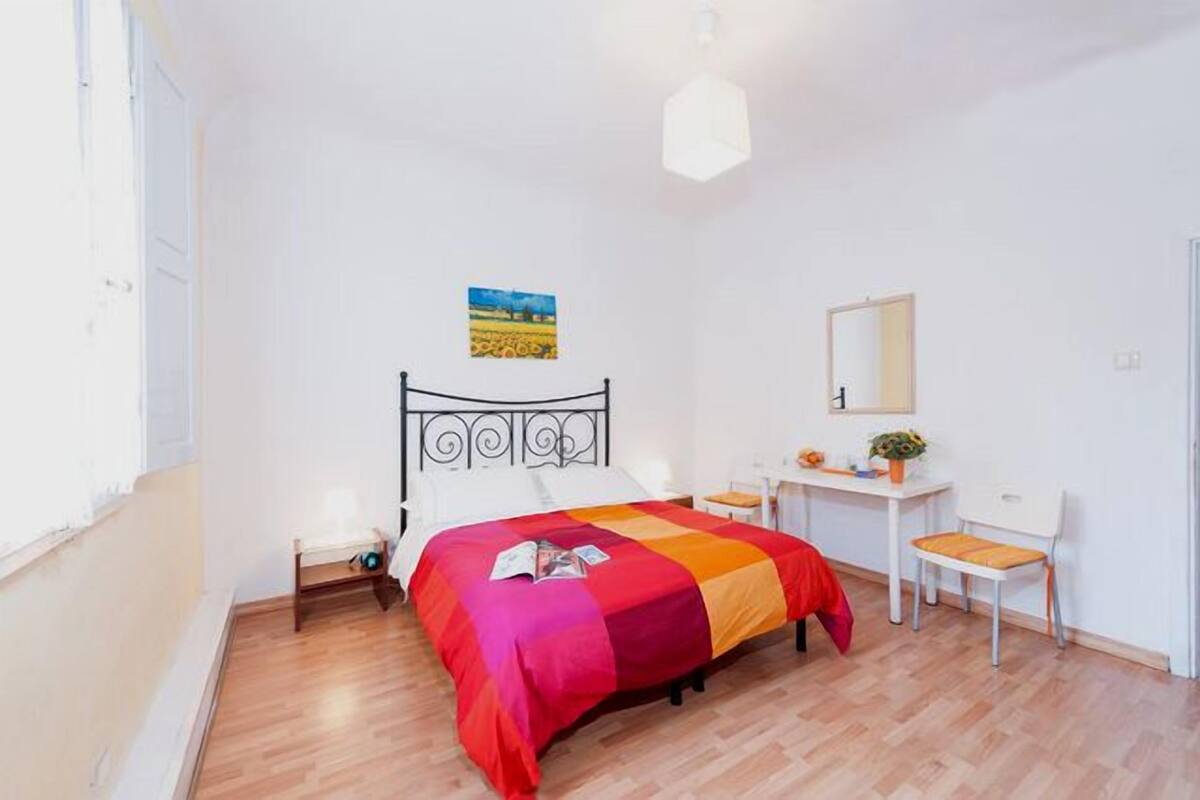 Une chambre à coucher comprenant un lit, une table de chevet, une chaise, un bureau et un tableau accroché au mur.