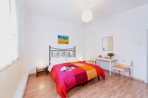 Une chambre à coucher comprenant un lit, une table de chevet, une chaise, un bureau et un tableau accroché au mur.