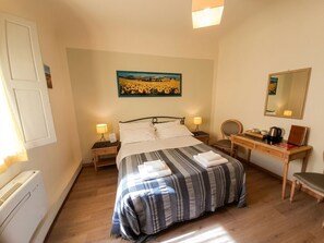 Een slaapkamer met een bed, nachtkastjes, een bureau, een stoel, een lamp, een spiegel en een schilderij aan de muur.