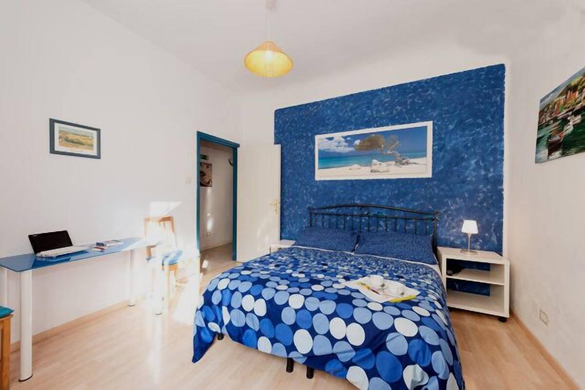 Une chambre à coucher comprenant un lit, un bureau, une chaise, une table de chevet et un mur orné d’un tableau.