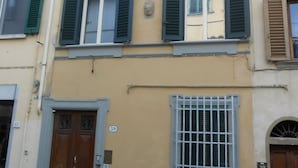 Un immeuble à plusieurs étages, doté d’une façade jaune, de volets verts et d’une fenêtre grillagée.
