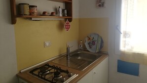 Een kleine keuken met een gasfornuis, een spoelbak en een plank met keukengerei.