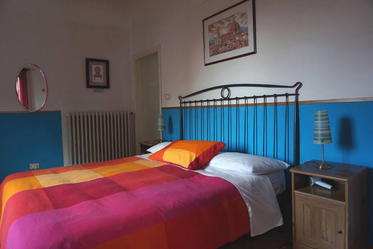 Une chambre d’hôtel avec un lit, une table de chevet, une lampe, un tableau encadré au mur et un radiateur.