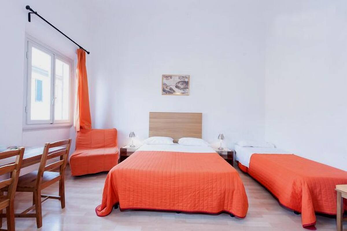 Une chambre d’hôtel comprenant un lit double, deux lits simples, un bureau, une chaise et une fenêtre avec des rideaux.