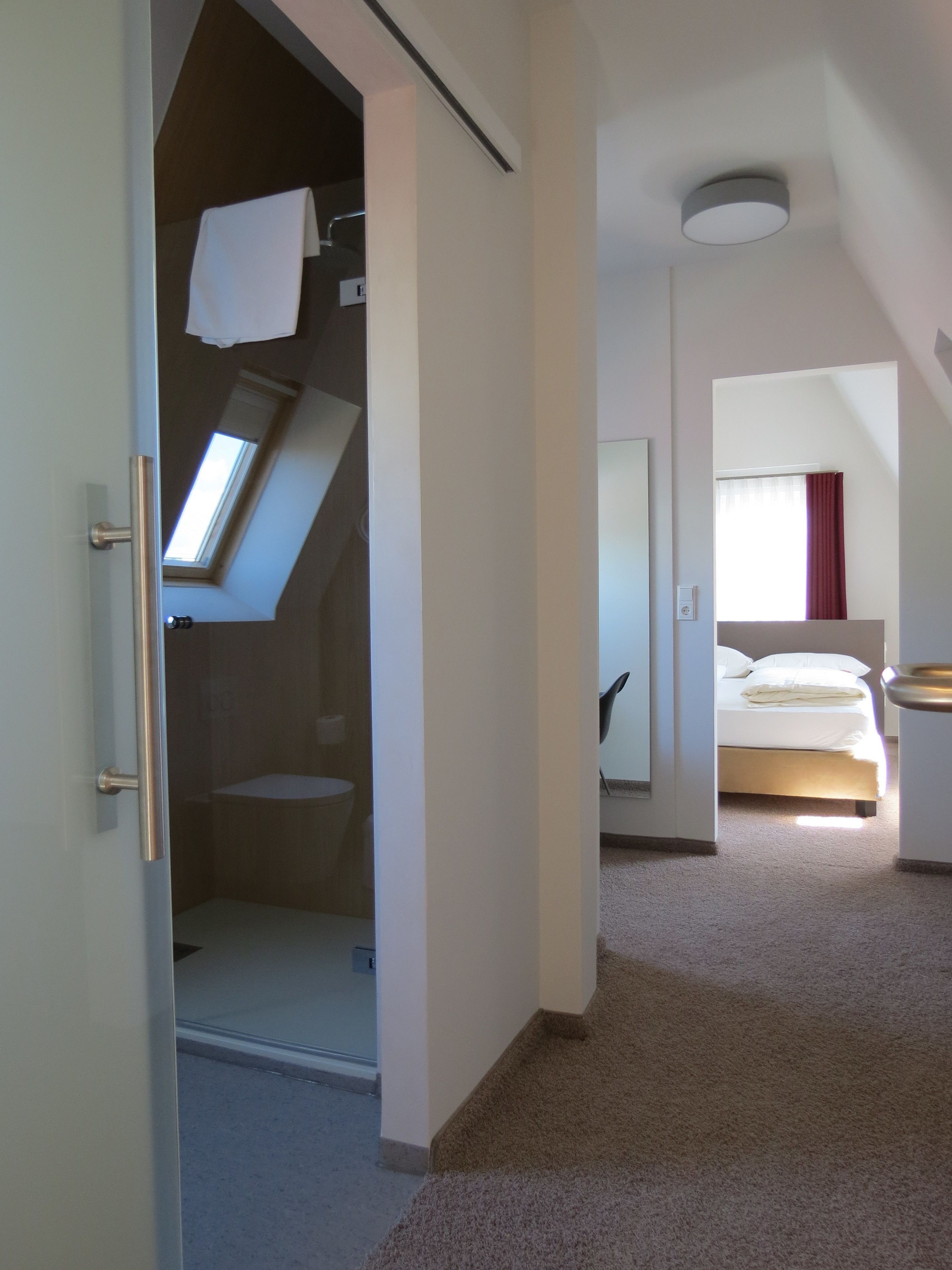 Une chambre d’hôtel avec une lucarne, un lit, une salle de bain et un petit coin salon.