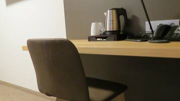 Una silla de oficina moderna, un escritorio con una cafetera, un teléfono y un monitor de computadora en la pared.