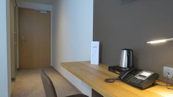 A hotel reception area with a wooden desk, a telephone, a kettle, and a signboard.