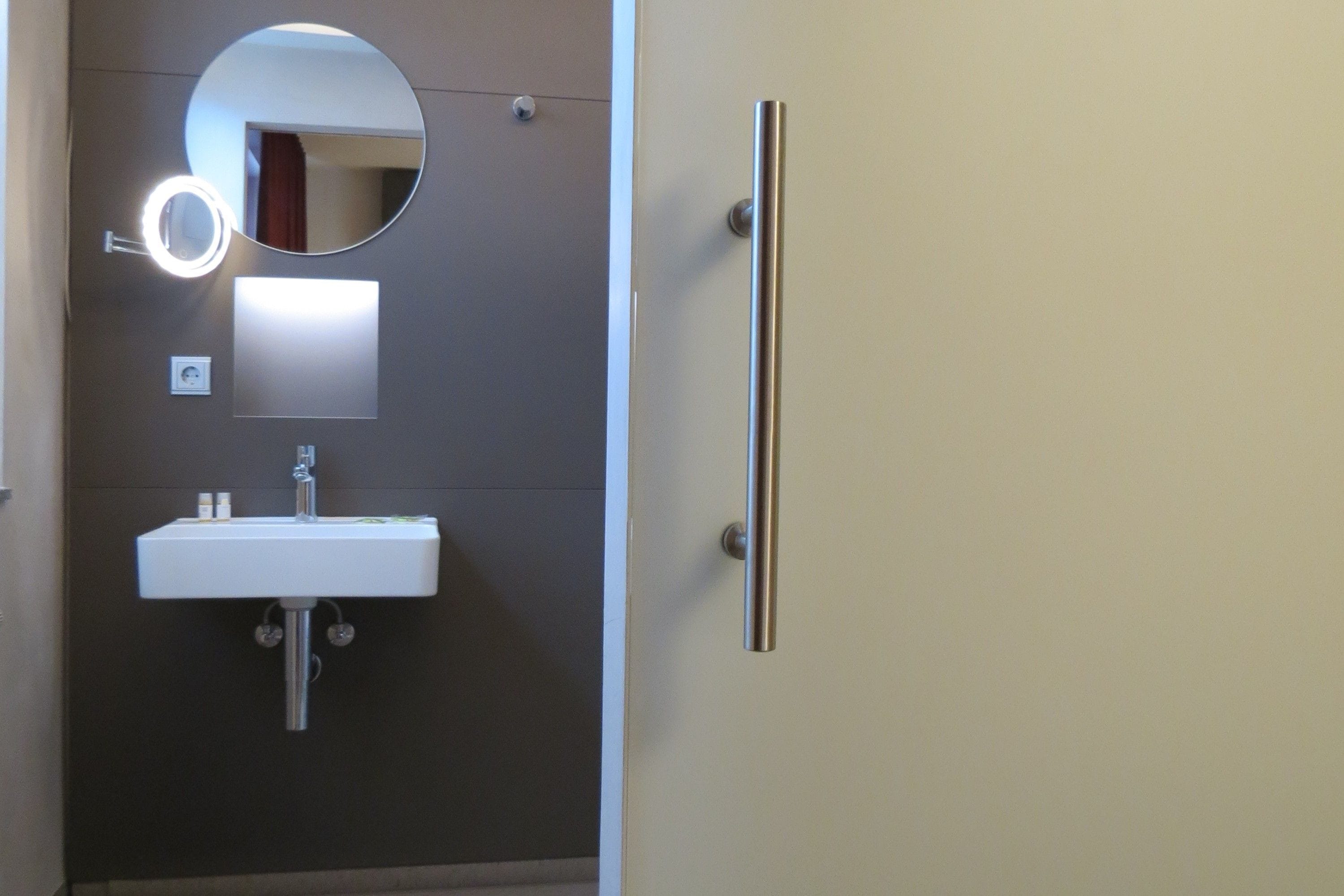 A bathroom with a white sink, a round mirror with a light, and a door with a vertical handle.
