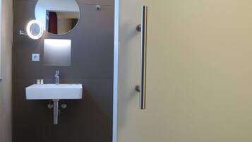 A bathroom with a white sink, a round mirror with a light, and a door with a vertical handle.