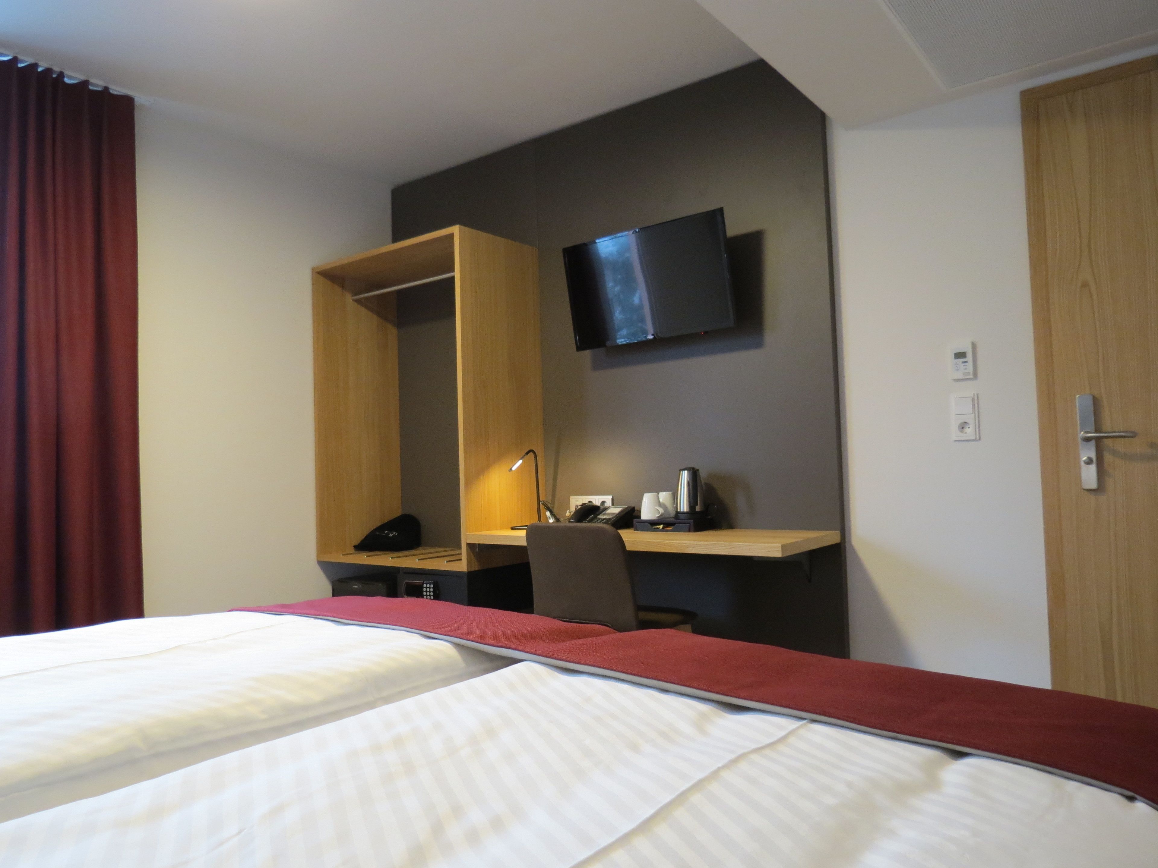 Habitació d'hotel amb dos llits, un escriptori amb cadira, un televisor fixat a la paret i un armari.