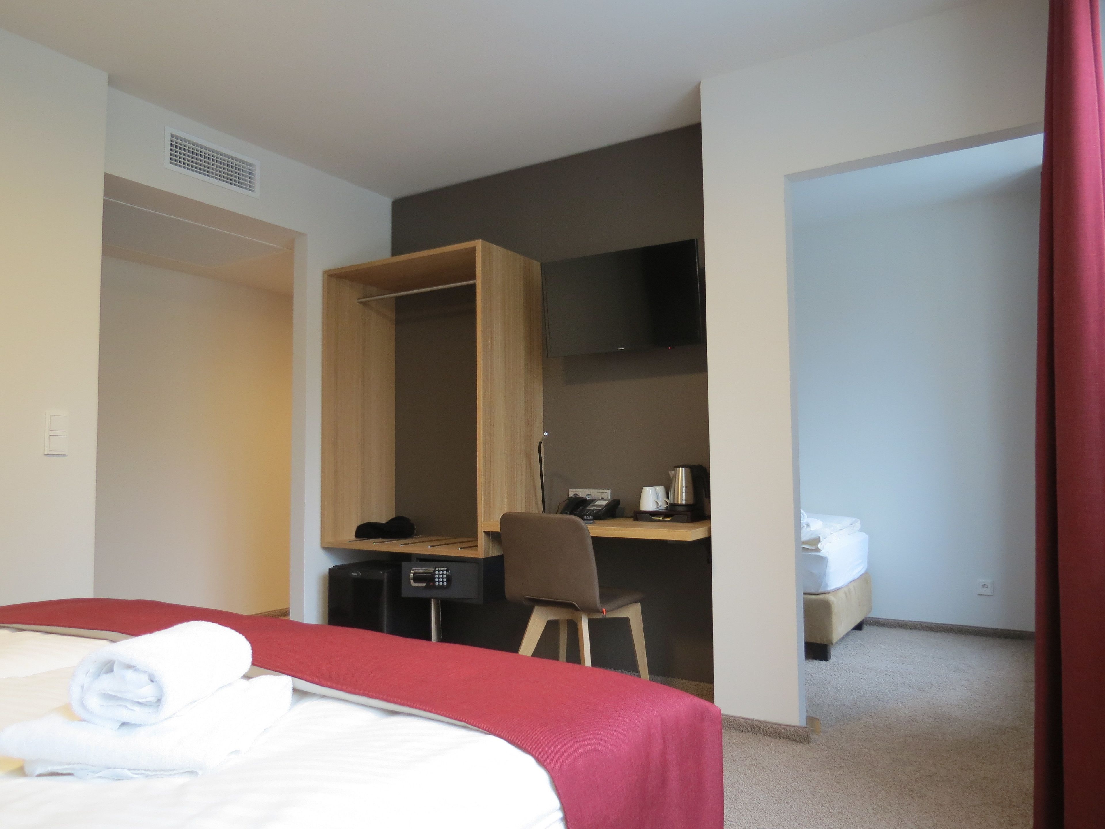 A hotel room with a bed, a desk with a chair, a TV, a coffee maker, and a toilet.