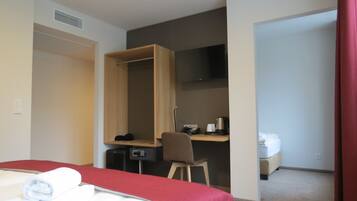A hotel room with a bed, a desk with a chair, a TV, a coffee maker, and a toilet.