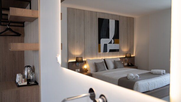 A modern hotel room with a large bed, bedside tables, a coffee maker, and a wall-mounted abstract painting. - Galaxy Hotel (Ierapetra)