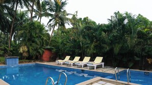 A swimming pool with tiled edges, surrounded by palm trees and lounge chairs.