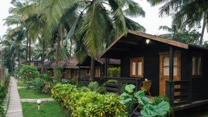 A row of wooden cabins with a garden path, surrounded by lush greenery and palm trees.