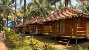 Wooden cabins with tiled roofs, surrounded by palm trees and small plants.