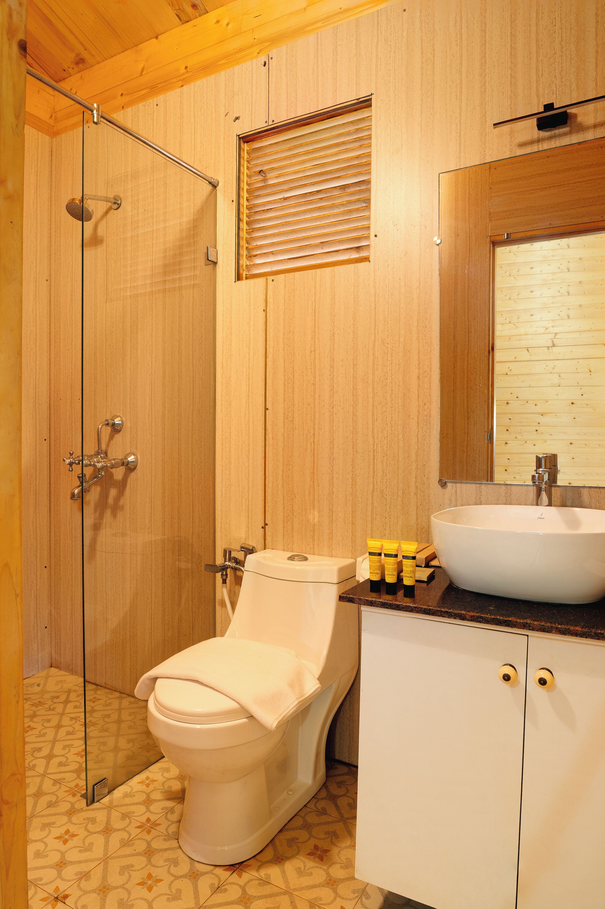 Une salle de bain aux murs lambrissés, dotée d’une douche en verre, de toilettes, d’un lavabo et d’un miroir au-dessus du lavabo.