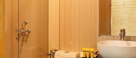 A wooden-paneled bathroom with a glass shower enclosure, a toilet, a sink, and a mirror above the sink.
