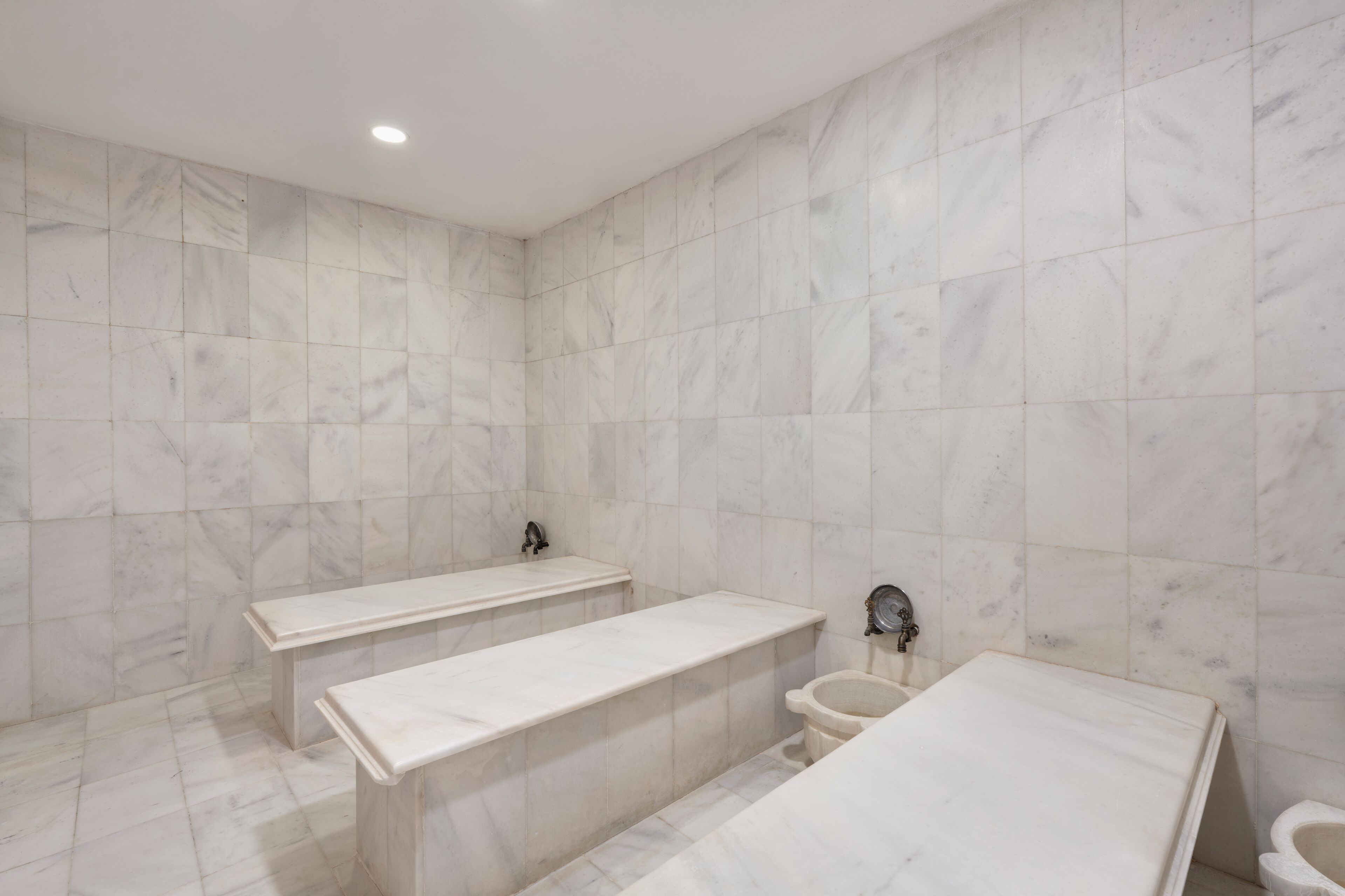 Een badkamer met marmeren wanden, een badkuip, een toilet en een bankje.