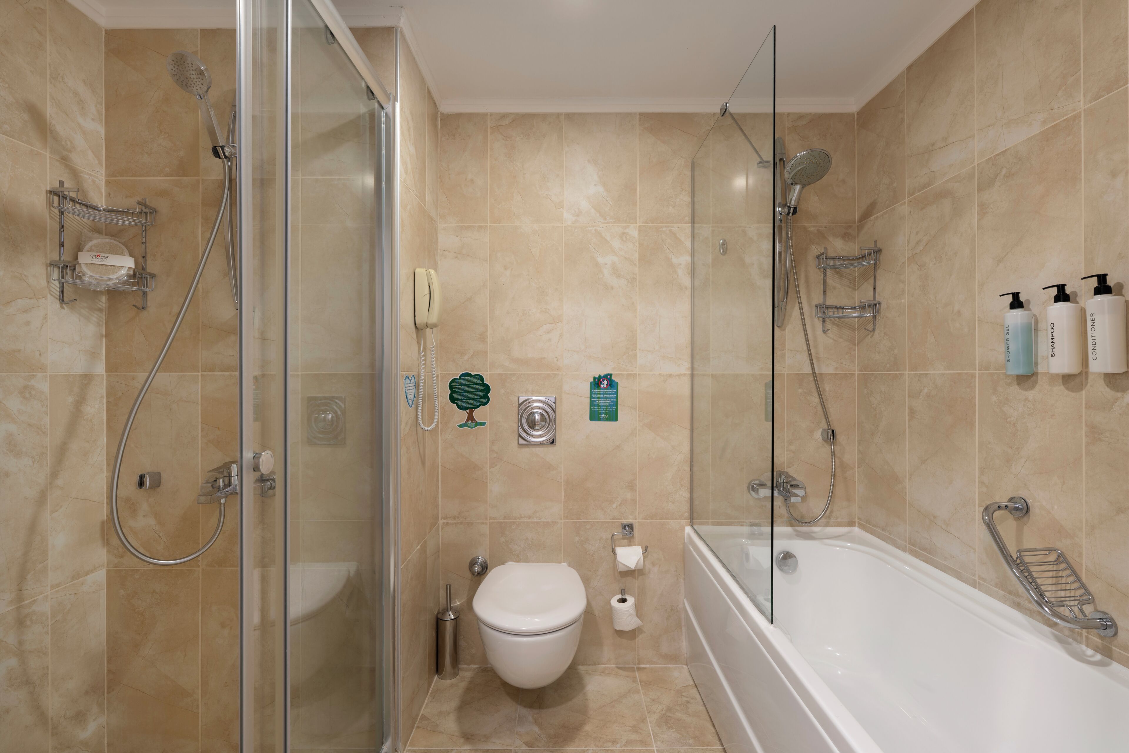 Un baño moderno con ducha de vidrio, inodoro, bañera y diversos artículos de aseo en la pared.