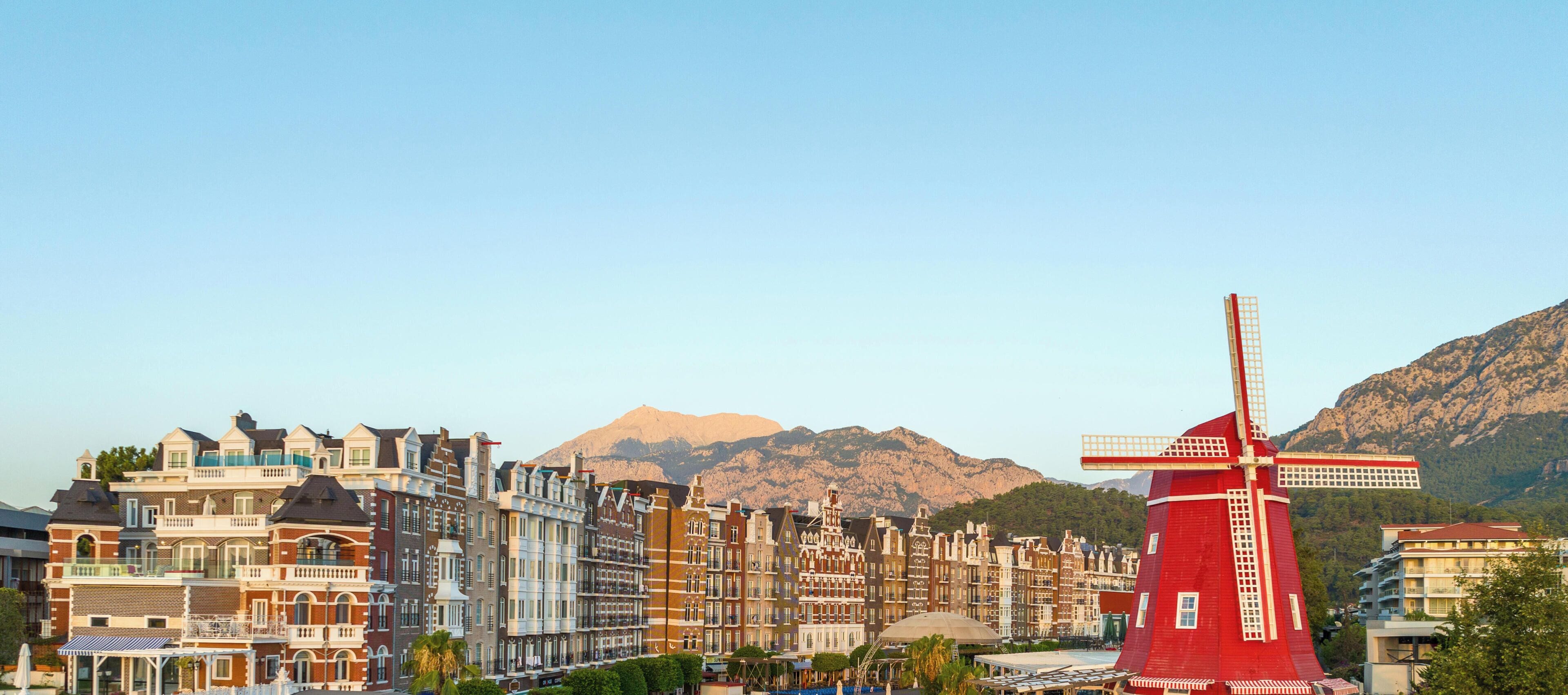 A red windmill in a town with historic buildings and mountains in the background.