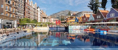 Una piscina con sillas de descanso, una montaña al fondo y arquitectura europea tradicional.