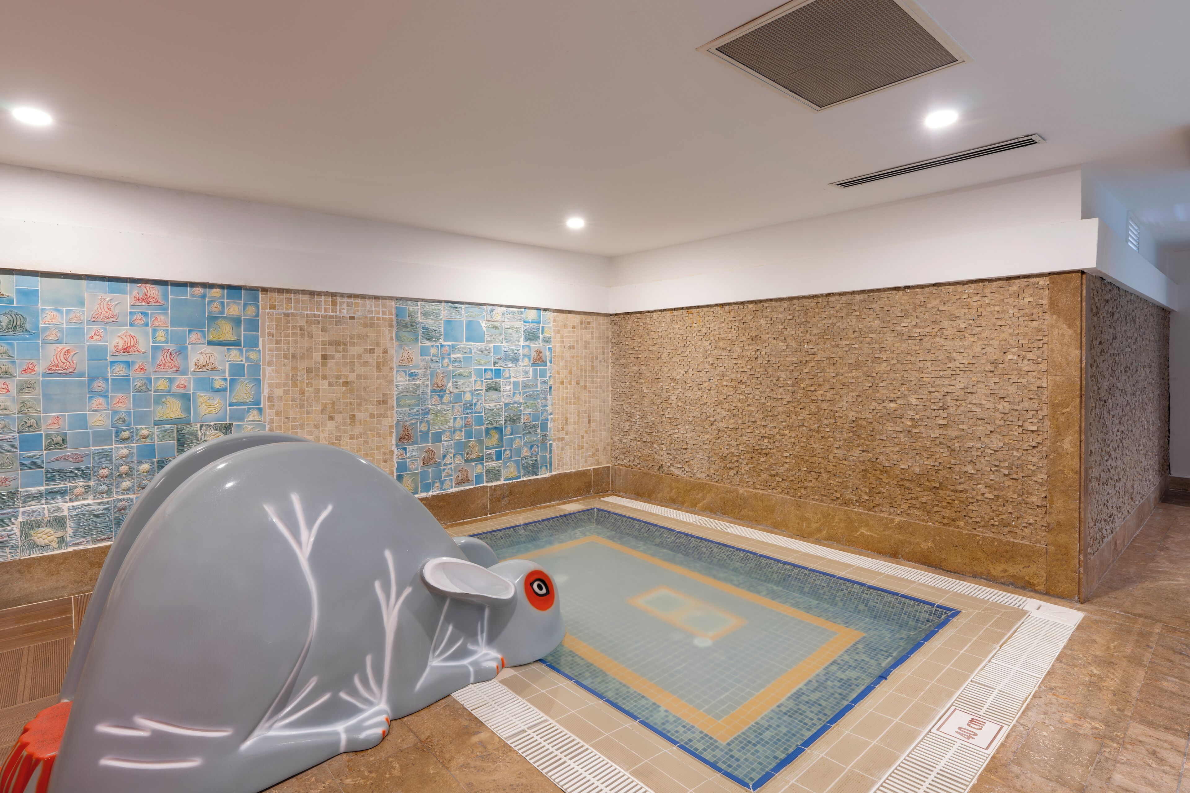 A swimming pool with a tiled wall, a brick wall, and a ceiling vent.