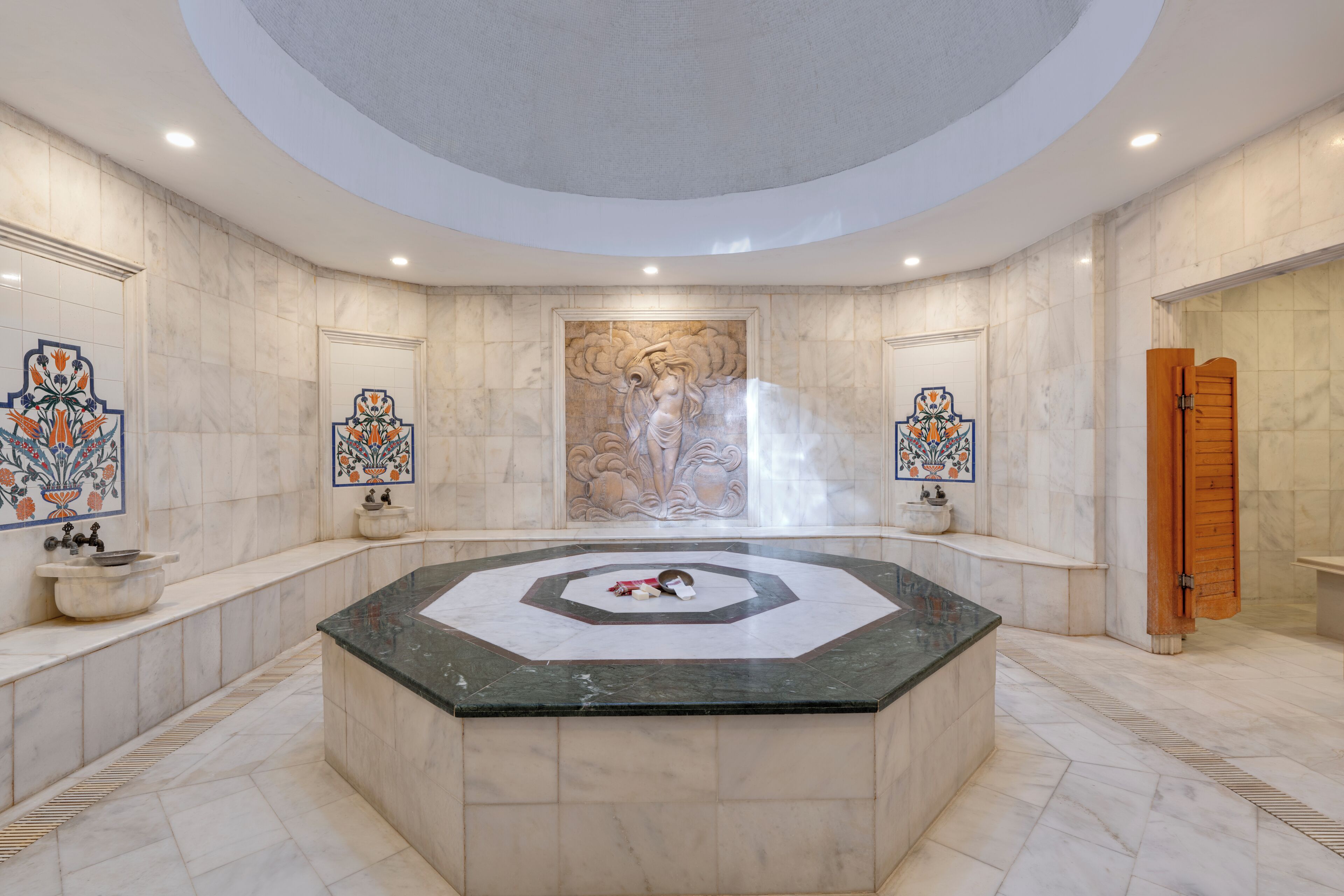 A luxurious bathroom with a central marble sink, decorative tiles, and a large mural on the wall.