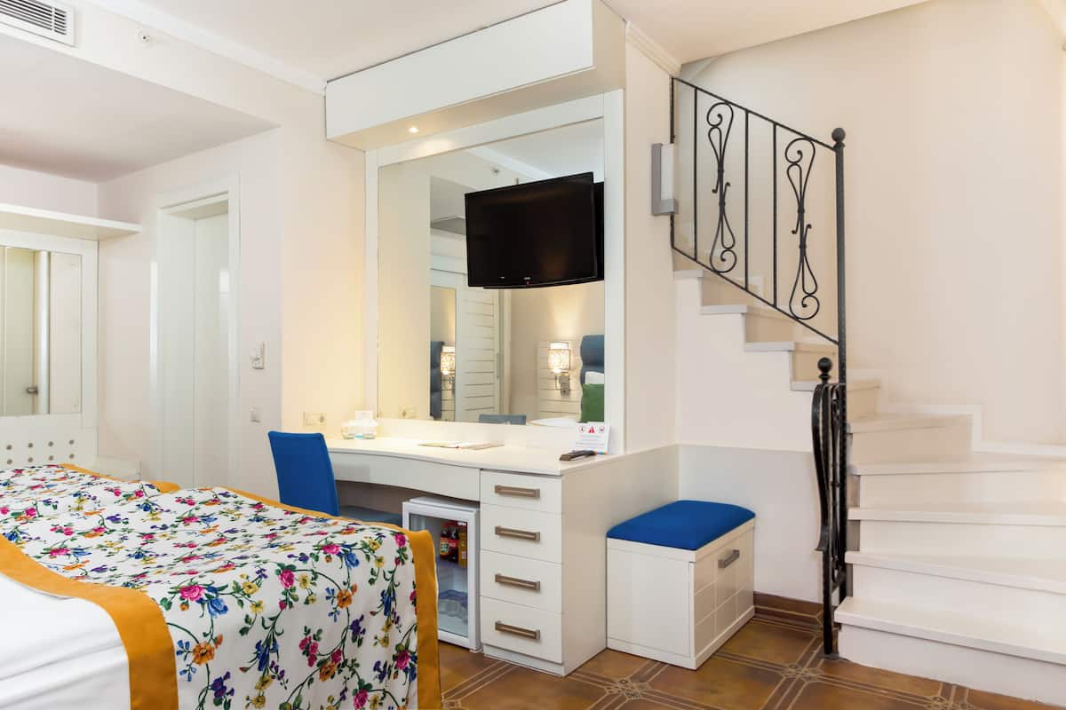 A bedroom with a bed, a desk, a chair, a TV, a mirror, and a staircase.