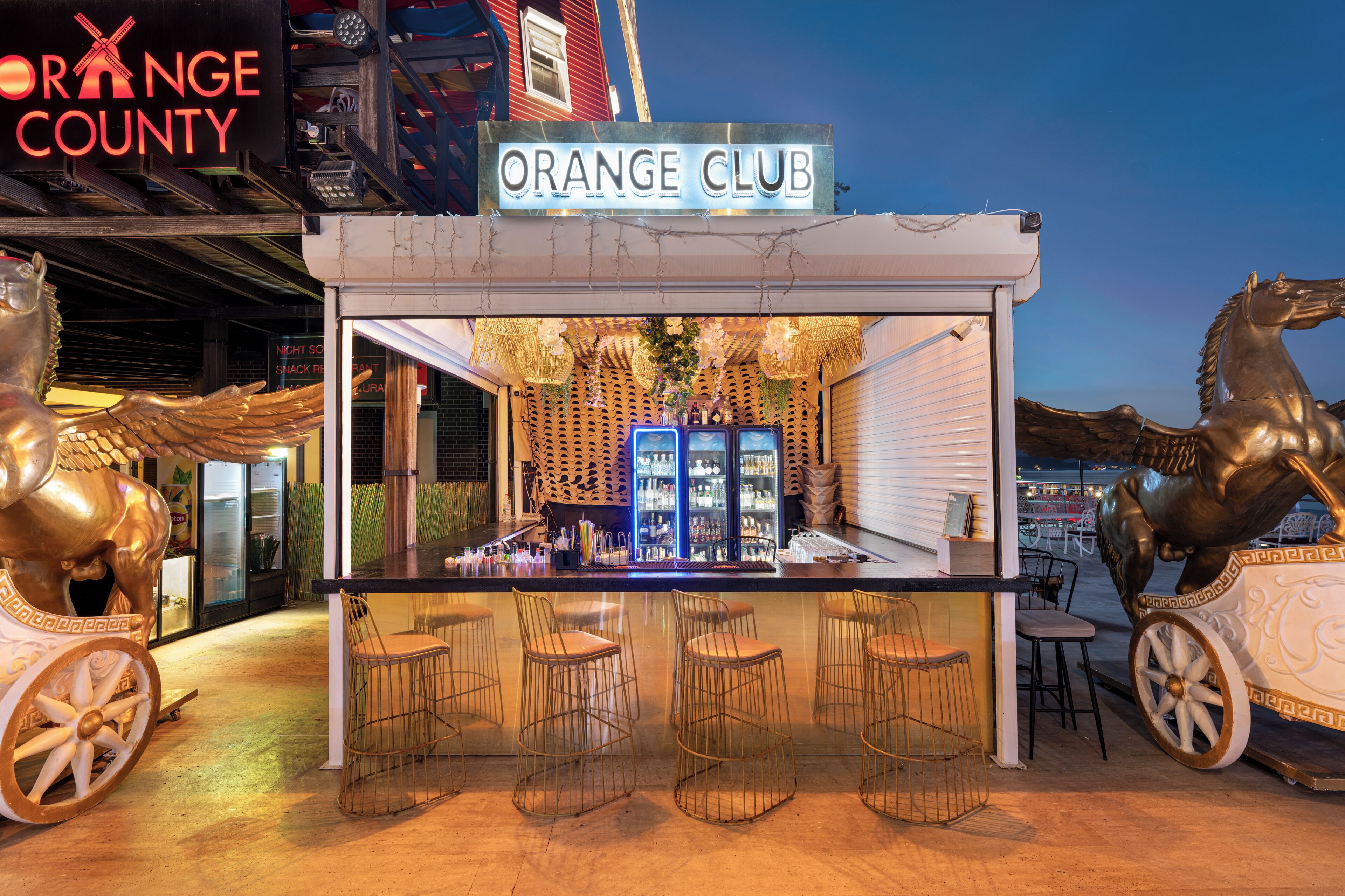 A bar named Orange Club with a sign, a counter, stools, and decorative horses.
