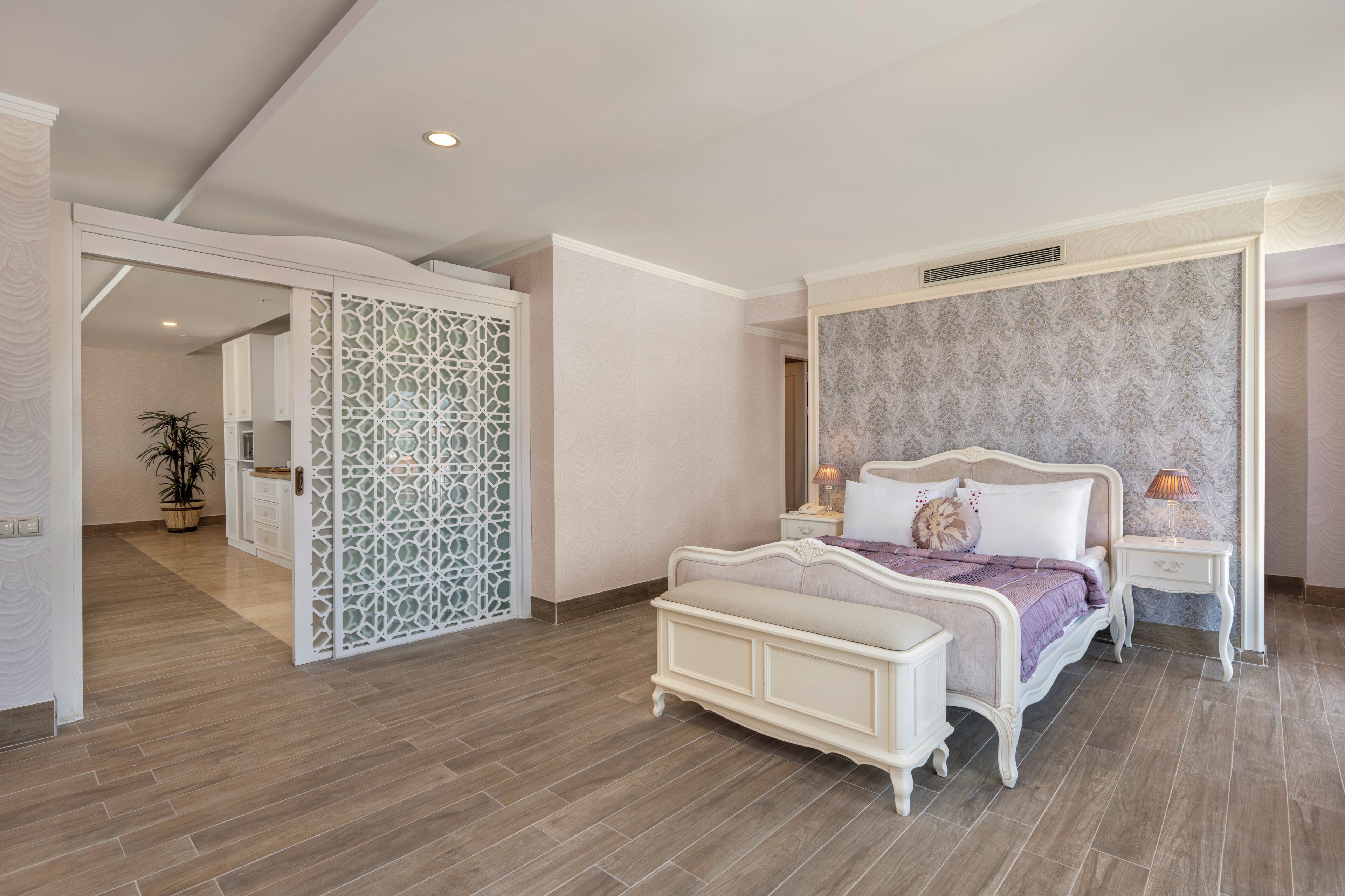 A bedroom with a bed, bedside tables, a decorative partition, and a potted plant.