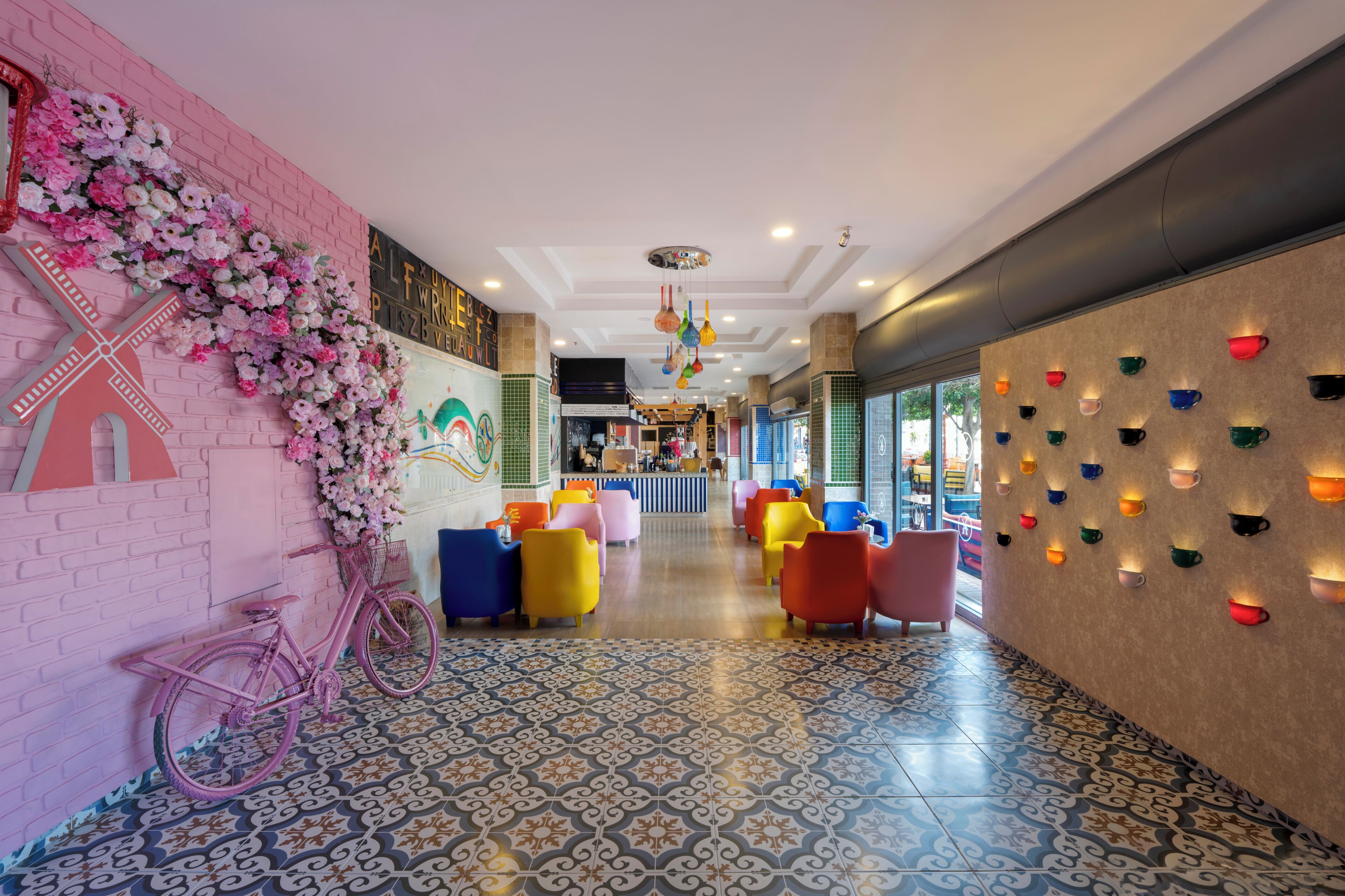 A hotel lobby with a pink brick wall, a bicycle, colorful chairs, a patterned floor, and wall-mounted lights.