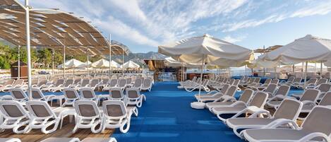 A sun deck with rows of lounge chairs and umbrellas, a wooden deck, and a view of the sea and mountains.