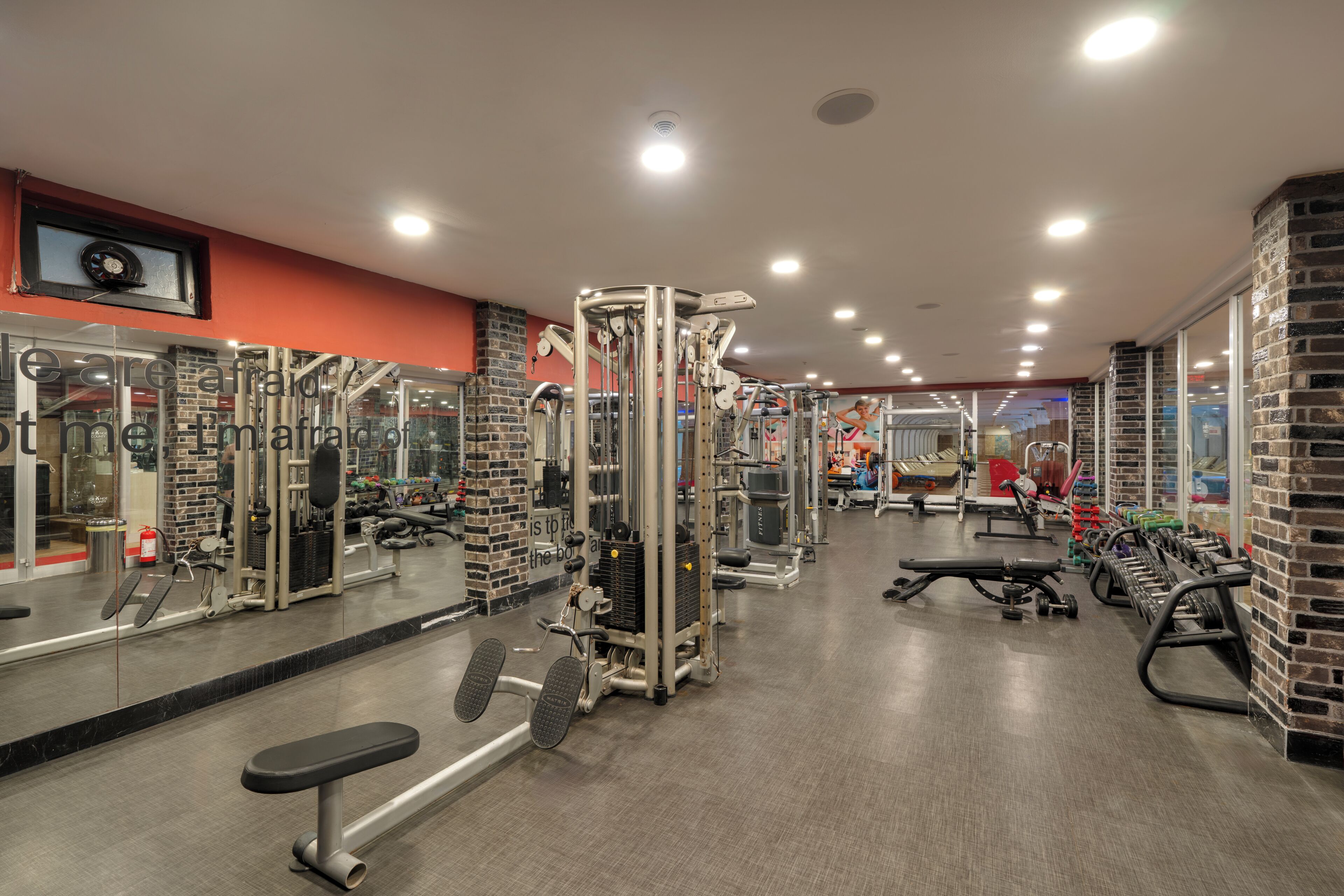 Ein Fitnessraum mit unterschiedlichen Trainingsgeräten, einem Spiegel und einer Ziegelwand.