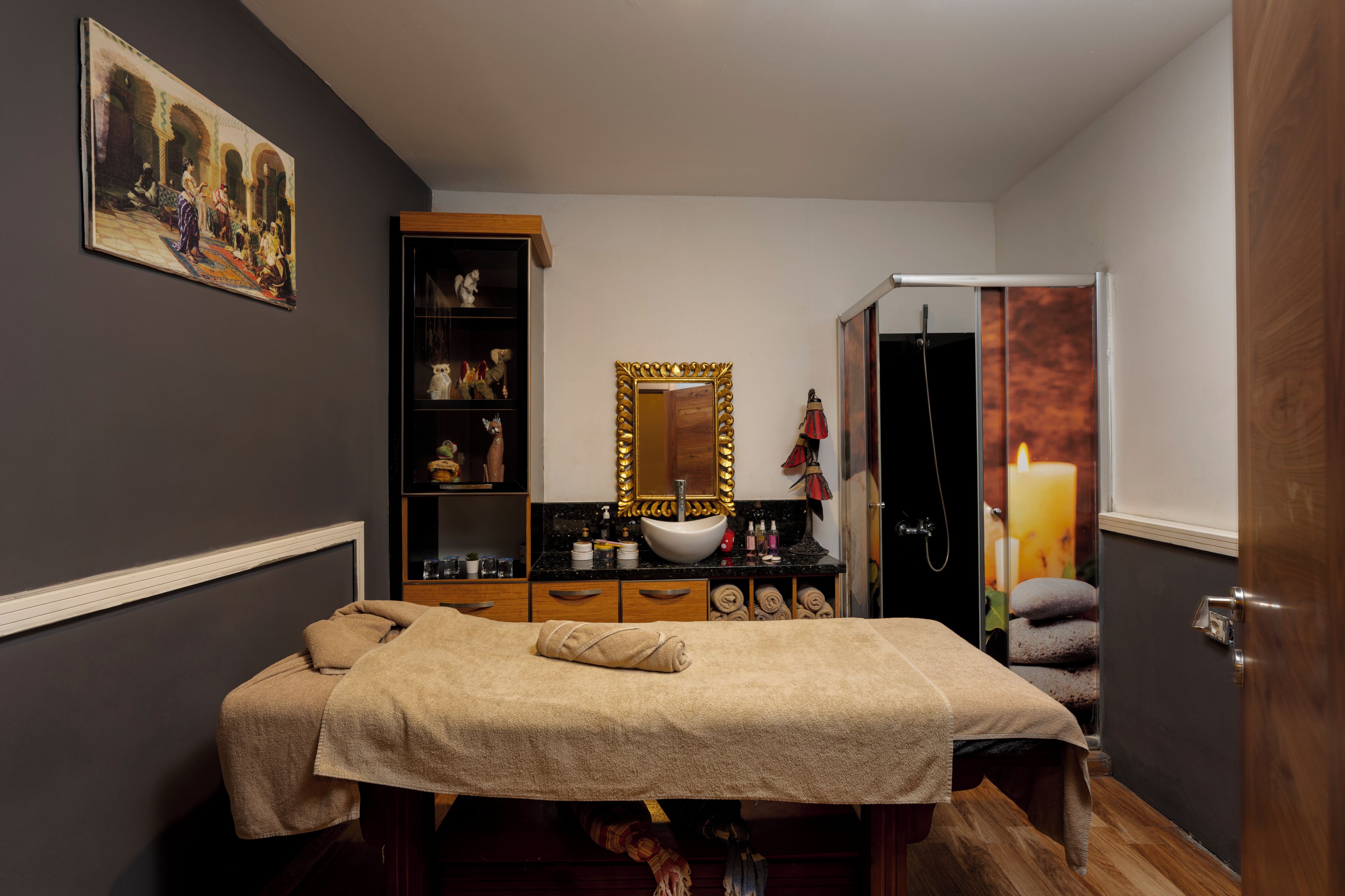 Un cuarto de spa con una camilla de masaje, un tocador con espejo y un estante con objetos decorativos.