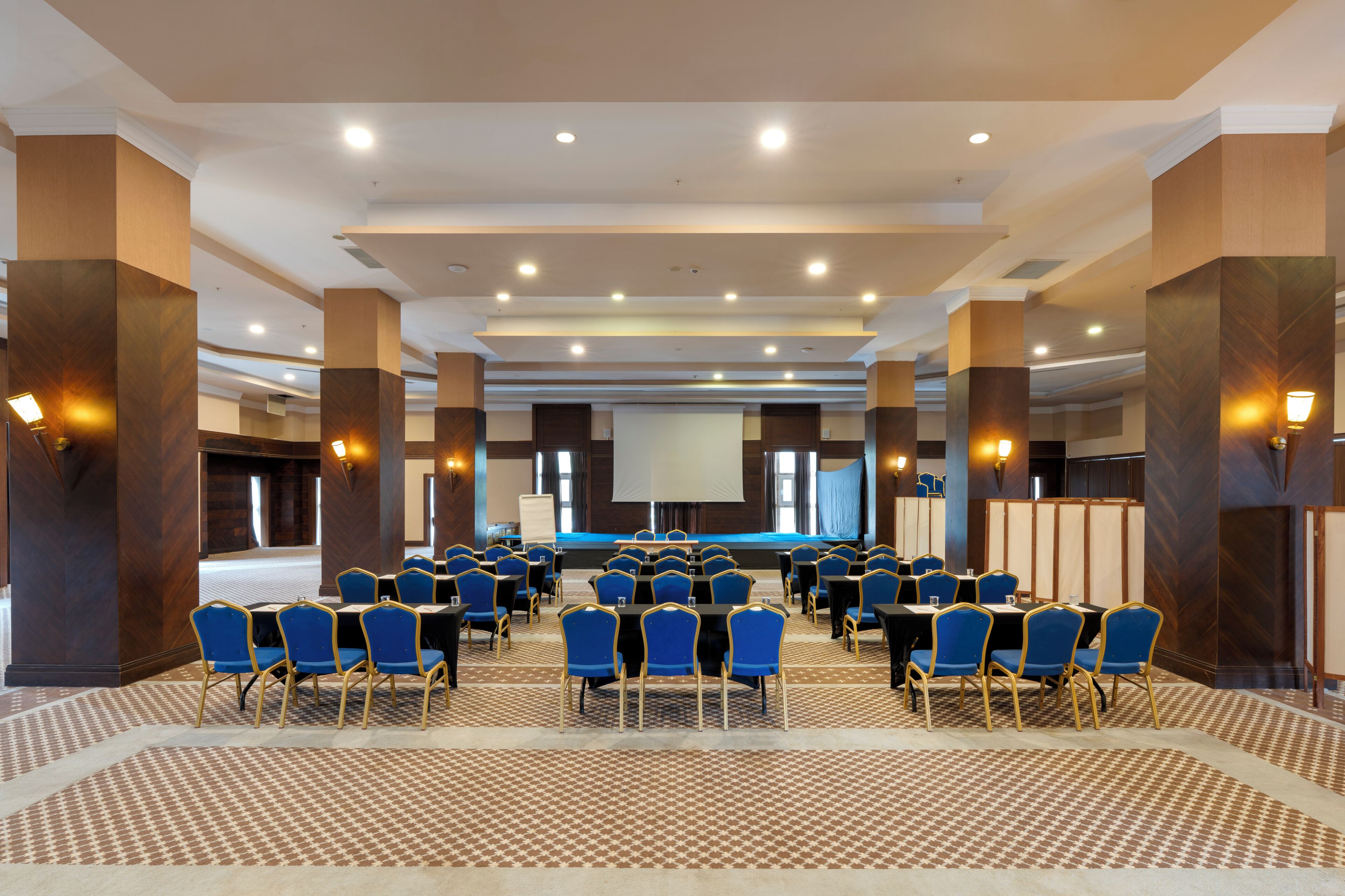 A conference room with rows of blue chairs, a stage, and a large screen.
