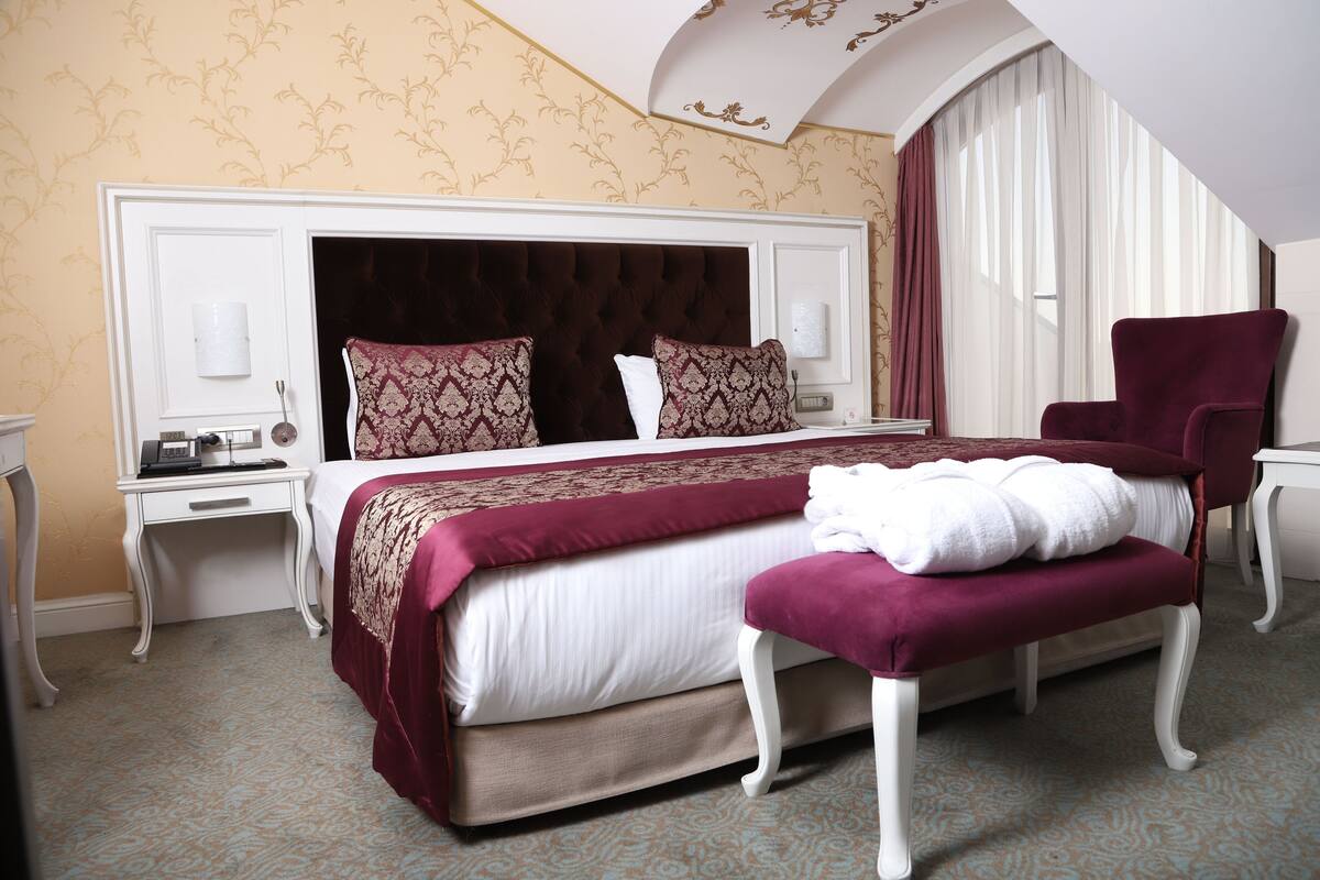 A hotel room with a large bed, a chair, a desk, and a window with curtains.