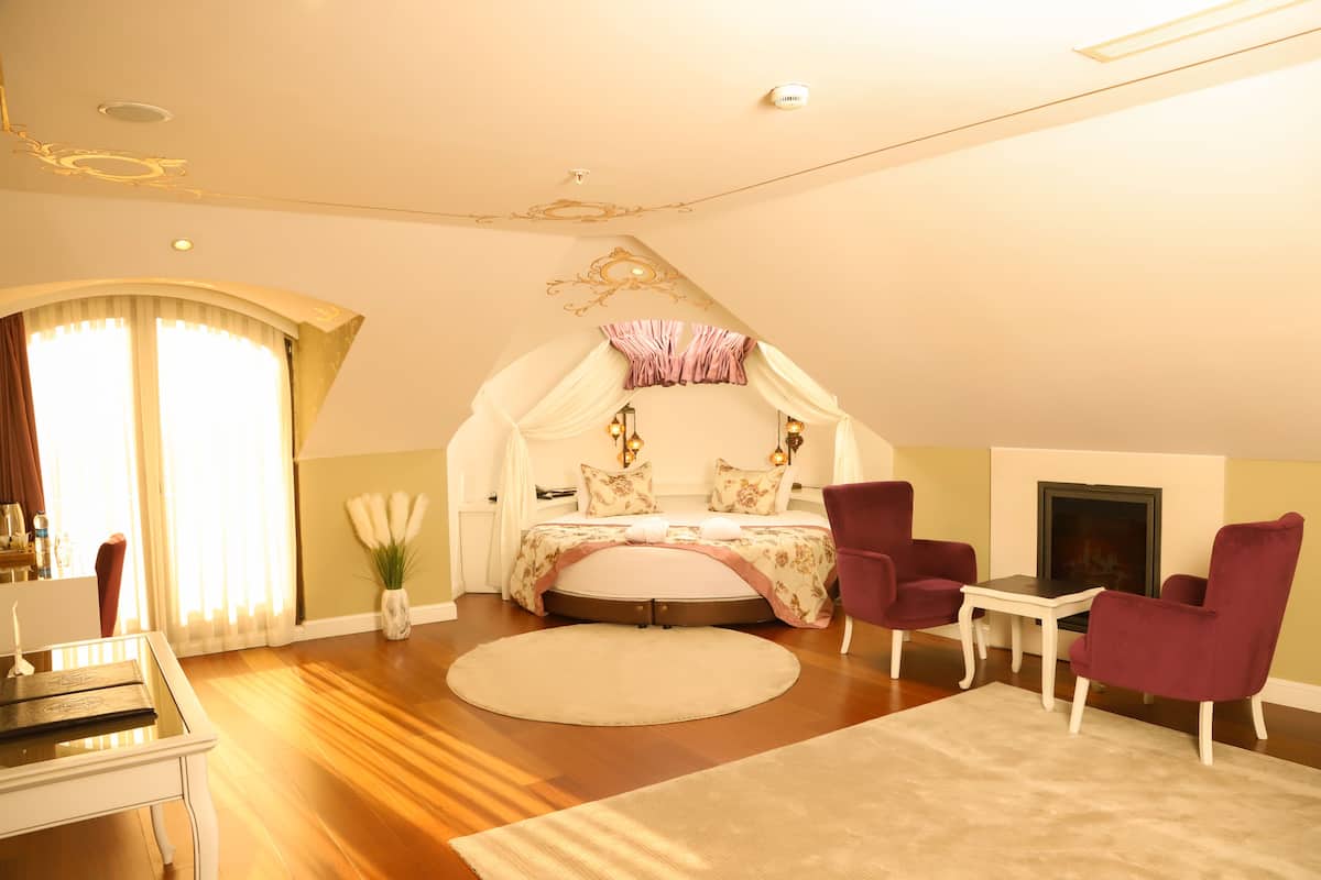A bedroom with a bed, two chairs, a small table, and a fireplace.