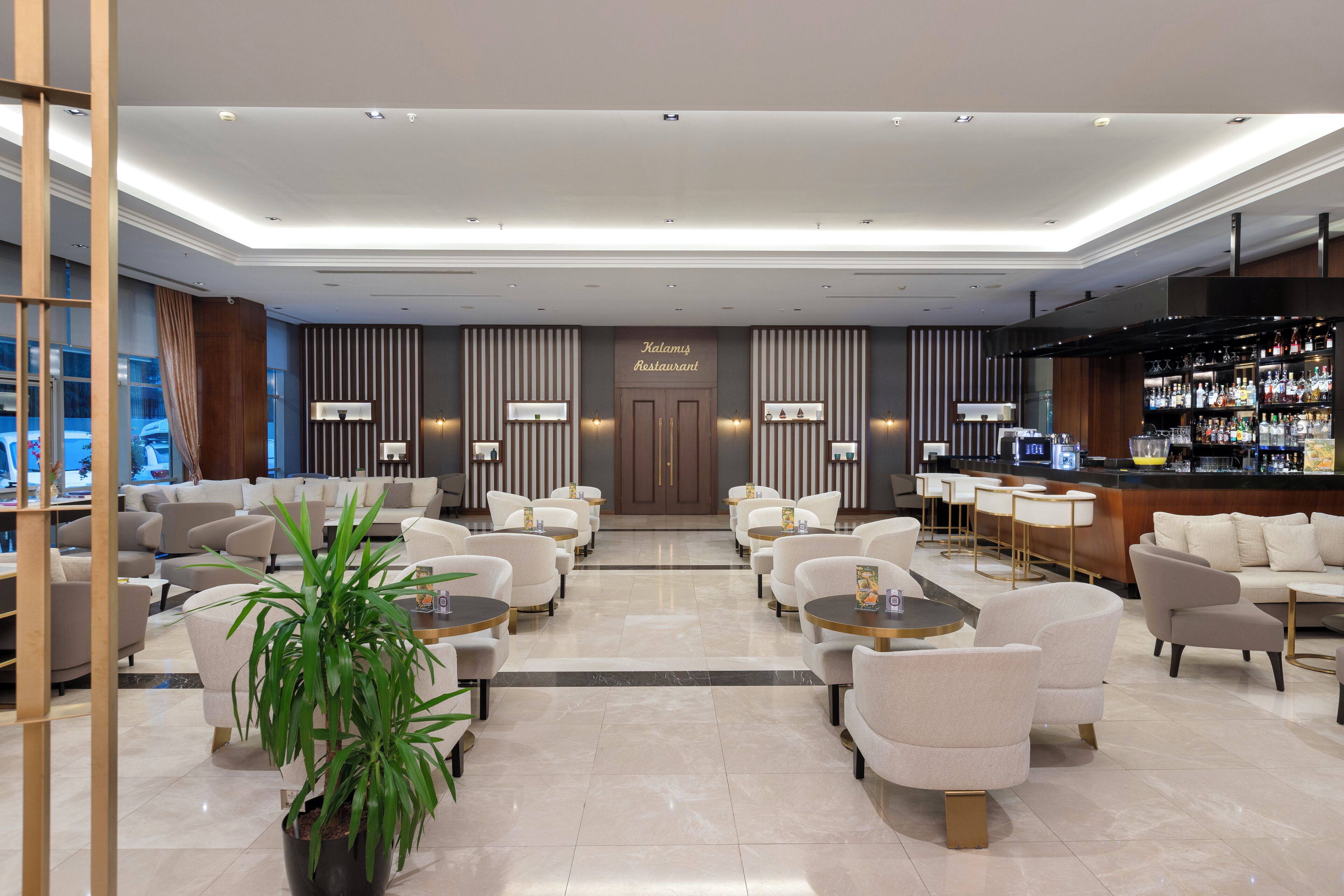 Un moderno vestíbulo de hotel con zona de bar, diferentes disposiciones de asientos y un mostrador de recepción.