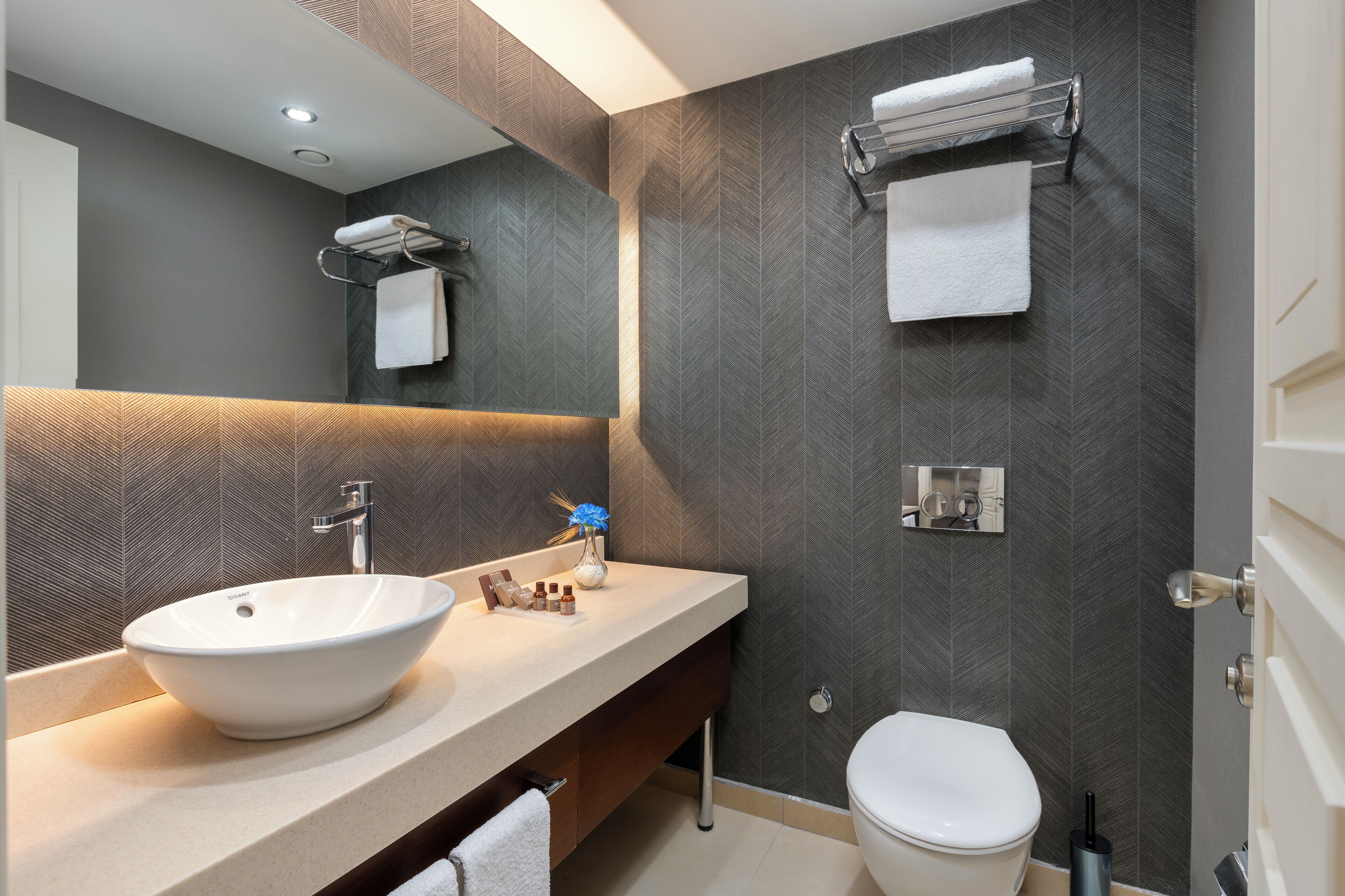 Un bagno moderno con lavabo a incasso, uno specchio, un portasciugamani e un water.