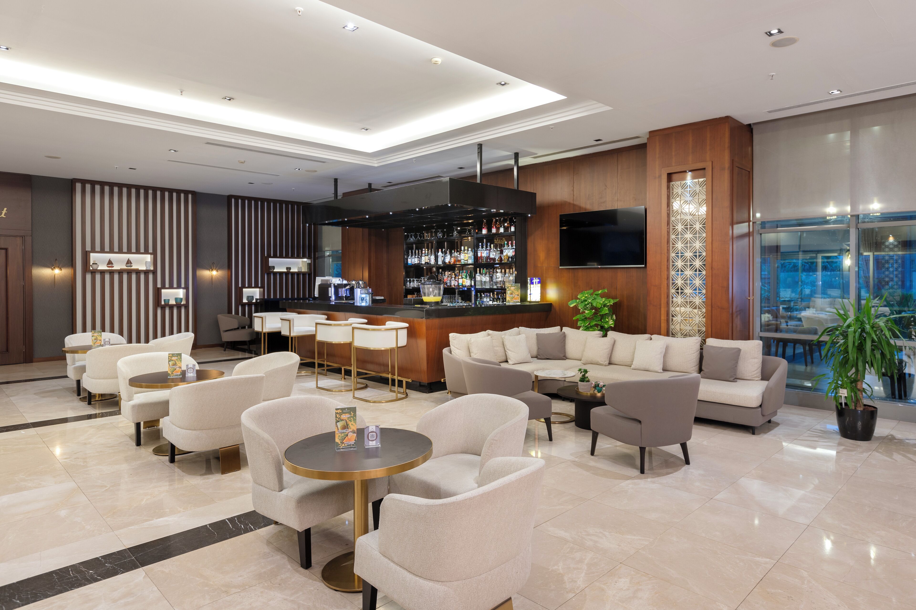 A modern lobby with a bar area, seating arrangements, and a large TV screen.