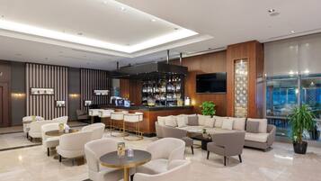 A modern lobby with a bar area, seating arrangements, and a large TV screen.
